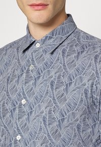 Overhemd met knopen in marineblauw en wit met een bladpatroon; heeft een puntige kraag en knoopsluiting; gemaakt van lichtgewicht stof.