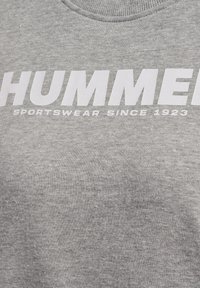 Gråt sportstøjsstof med stor hvid tekst "HUMMER" og mindre tekst "SPORTSWEAR SINCE 1923" under halsudskæringen.