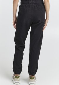 Black linen jogger pants with elastic waist and cuffs, featuring side and back pockets, paired with light-colored sneakers.