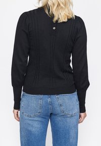 Pull en maille noir avec un design à côtes verticales, encolure ronde et trois boutons au dos. Associé à un jean taille haute bleu clair.