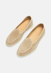 Zapatillas de ante beige sin cordones con punta afilada, borde blanco y un interior suave. Suela flexible con características de diseño mínimas.