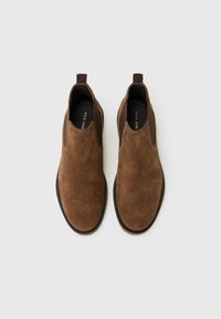 Zapatos de ante marrón tipo slip-on con paneles elásticos en los laterales, punteras redondeadas y suelas texturizadas. Presentan una pestaña para facilitar su colocación.