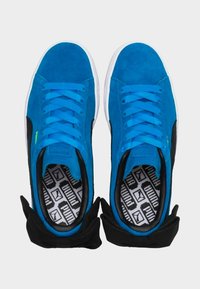 Blå mockaskor med svarta accenter, med platt snörning, en texturerad sula och en mönstrad innersula.