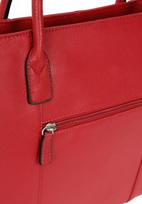 Rode leren handtas met een gladde textuur, voorzien van een ritsvak en stevige handvatten. Accenten zijn zwarte stiksels en ritshardware.