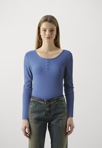 Body a maniche lunghe in maglia a coste di colore azzurro chiaro, con scollatura rotonda e bottoncini, abbinato a jeans in denim chiaro a vita alta.