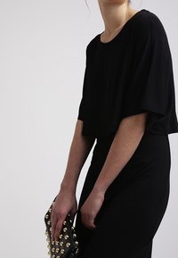 Černý zkrácený top s širokými rukávy, kombinovaný s dobře padnoucí černou sukní. Doplňkem je černá kabelka na ruku zdobená zlatými hroty.