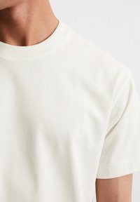 Light-colored cotton short-sleeve t-shirt featuring a ribbed crew neckline. Smooth, soft texture with a simple design and no visible patterns.