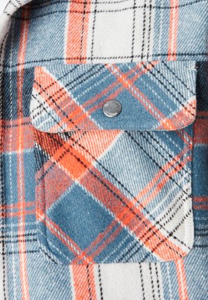 Poche de chemise en flanelle avec un motif à carreaux orange, bleu et blanc, dotée d'un rabat fixé par un bouton-pression métallique.