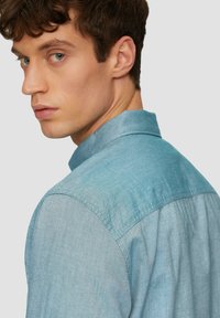 Lichtblauwe denim overhemd met een klassieke kraag en knoopsluiting, met een licht vervaagde textuur en gestikte accenten op de schouders.