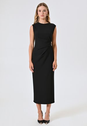 Robe midi sans manches noire avec un détail tordu asymétrique et des accents dorés. Tissu lisse, silhouette ajustée et design longueur cheville.