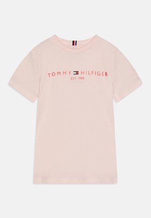 Jasnoróżowy t-shirt z krótkim rękawem z napisem „Tommy Hilfiger EST. 1985” oraz logo marki w kolorze czerwonym i granatowym na wysokości klatki piersiowej.