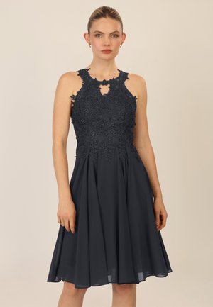 Dunkelmarineblaues Kleid mit einem enganliegenden Spitzenoberteil, gewelltem Ausschnitt und Schlüsselloch-Ausschnitt; fließender Rock aus leichtem Material.