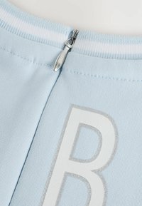 Hellblaues Stoffmaterial mit einer glatten Textur, ausgestattet mit einem silbernen Reißverschluss und einem weißen aufgedruckten Buchstaben "B" auf der Rückseite.