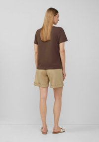Bruin t-shirt met korte mouwen, gecombineerd met beige opgerolde shorts, gemaakt van lichte stof. Slippers maken de casual look af.