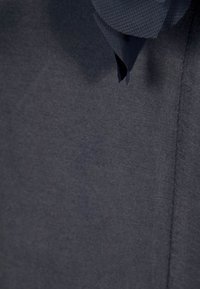 Tessuto grigio scuro con una texture liscia, caratterizzato da un nastro piegato nella parte superiore. Il design è minimalista con bordi puliti.