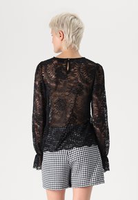 Black lace top with long sleeves, floral pattern, and keyhole back detail, paired with black and white checkered shorts.