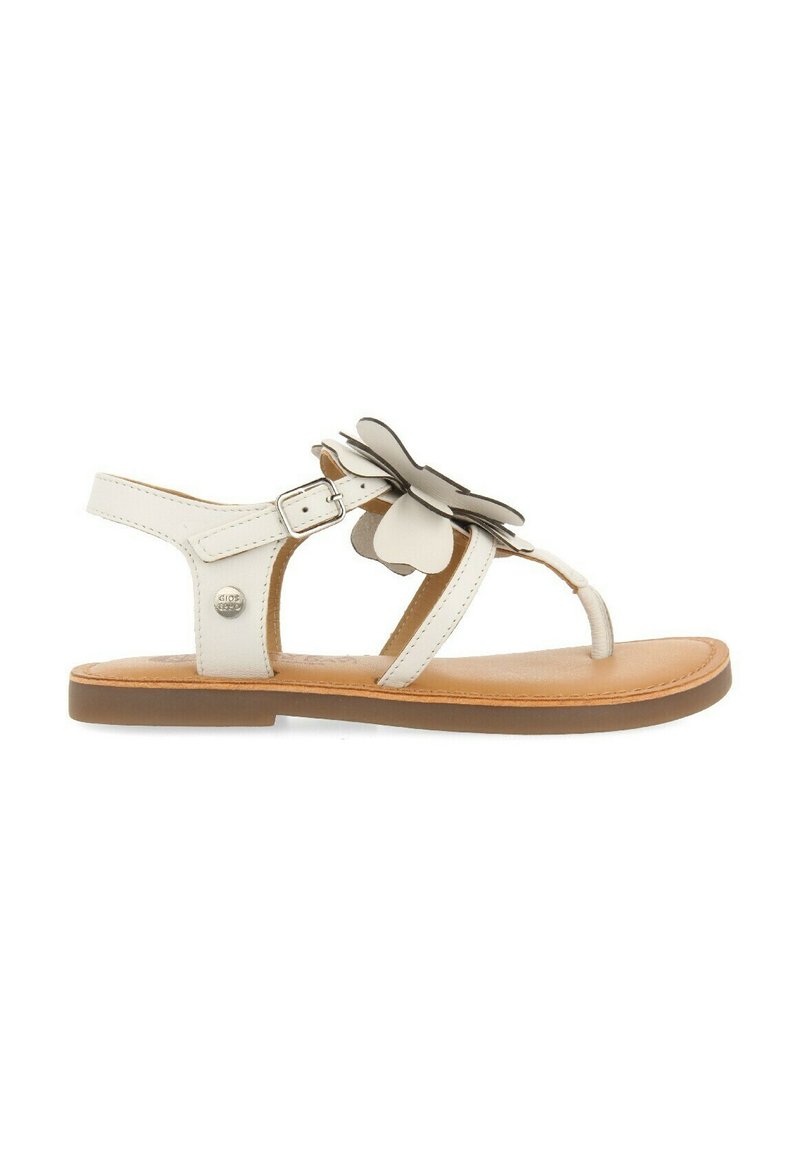 Sandalia de cuero blanca con un acento floral, correa ajustable en el tobillo y suela plana marrón. Presenta un diseño minimalista y una textura suave.