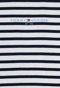 T-shirt rayé avec des bandes horizontales bleu marine et blanches. Présente le logo "TOMMY HILFIGER" en bleu, avec "EST. 1985" en dessous. Matériau en coton.