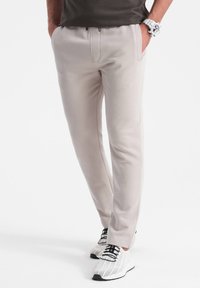 Helle beige Jogginghose mit taillierter Passform, ausgestattet mit frontalen Taschen und einem Kordelzugbund. Kombiniert mit weißen und schwarzen strukturierten Sneakers.