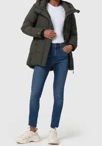 Doudoune vert olive avec capuche, fermeture éclair et boutons-pression, poches latérales, associée à un jean skinny bleu et des baskets blanches.