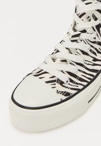 Svart og hvitt sebra-mønster lær høy-top sneakers med hvit gummitopp og såle, med flate hvite snører og detaljert hull.