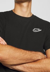 Svart bomullströja med rund hals, som har en vit Nike-logotyp på vänster bröst. Kortärmad och figurnära design.