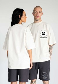 T-shirt cream oversize con una grafica nera sulla tasca frontale; abbinato a pantaloni corti neri con un dettaglio ricamato circolare.