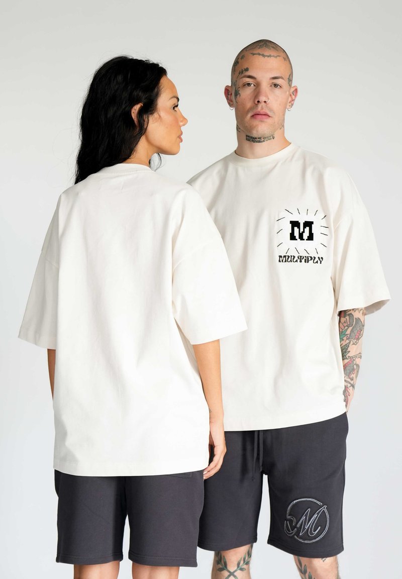 T-shirt cream oversize con una grafica nera sulla tasca frontale; abbinato a pantaloni corti neri con un dettaglio ricamato circolare.