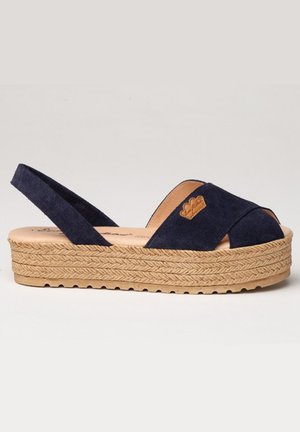 Sandalia cuña de ante azul marino con punta abierta, diseño entrelazado, suela de yute trenzado y detalles en cuero con logotipo.