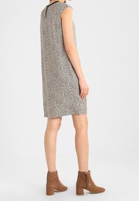 Ärmlös klänning med ett beige och svart abstrakt mönster, med en design med nyckelhål på baksidan. Kombineras med bruna ankelstövlar med dragkedja.