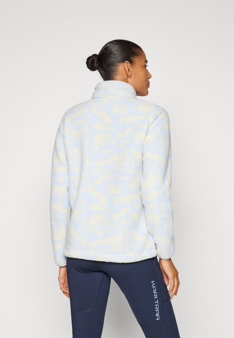 Fleecejacke in lichtblauw met een gemêleerd patroon en hoge kraag; bevat zacht materiaal en een relaxte pasvorm. Gecombineerd met marineblauwe leggings.