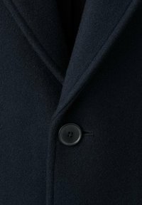 Abrigo de lana azul marino con solapa con muesca, que presenta un solo botón negro de plástico y una superficie suave y texturizada. Vista en primer plano de la tela.