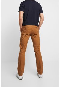 Brown cotton pants with a straight leg design, back pockets, and a smooth texture, paired with a navy t-shirt and white sneakers.