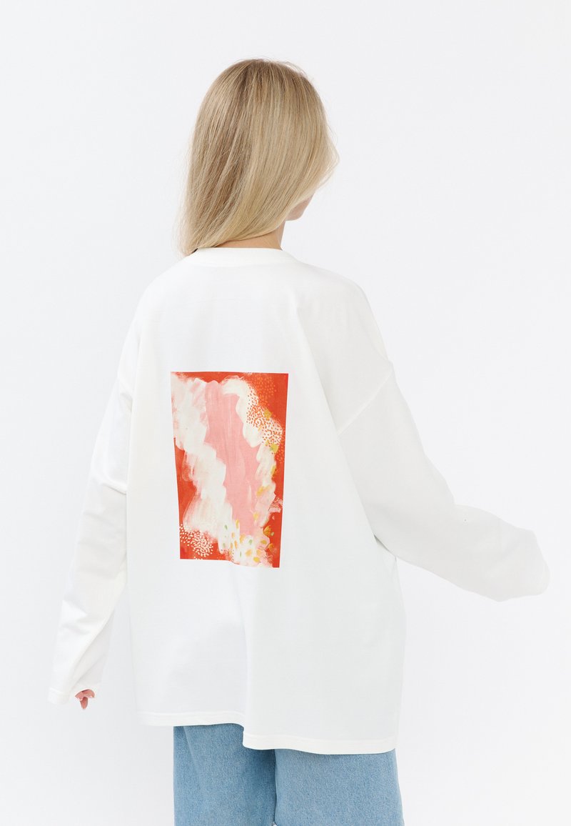 Witte blouse met lange mouwen, versierd met een groot kleurrijk abstract ontwerp op de achterkant in tinten oranje, roze en textuurpatronen.