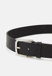 Czarny skórzany pasek z metalową klamrą w kolorze srebrnym, gładka tekstura, kilka otworów do regulacji i małe logo "BOSS" blisko klamry.