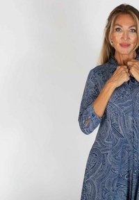 Niebieska sukienka w wzór paisley z kołnierzykiem, długimi rękawami z otworami i zwiewnym krojem. Wykonana z lekkiego materiału.