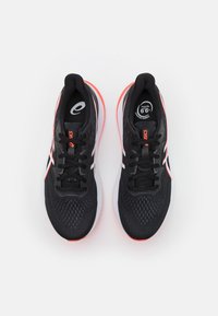 Zapatillas deportivas negras con una parte superior de malla transpirable, acentos en blanco y naranja neón, logotipo redondo y suela texturizada para tracción.