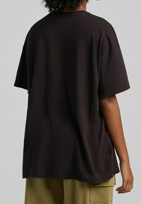 Musta puuvillainen t-paita rennolla istuvuudella, tippuneilla hihoilla ja pyöreällä kaula-aukolla. Sileä rakenne, ei näkyviä kuvioita tai koristuksia.