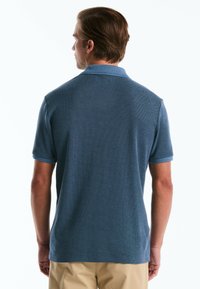 Polo à manches courtes pour homme en tissu bleu texturé, avec un col et des poignets bleu clair. Le design est ajusté avec un ourlet droit.