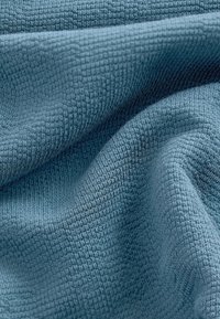 Tessuto testurizzato in un morbido colore blu, caratterizzato da un motivo intrecciato con elementi in rilievo sottili, creando un effetto 3D e profondità.