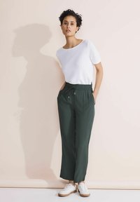 Pantaloni a gamba larga verde scuro realizzati in materiale leggero, con una vita elastica e cordino, abbinati a una maglietta bianca a maniche corte.