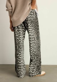 Weite Hosen im Leopardenmuster in Schwarz und Weiß, aus einem weichen Stoff mit einer hohen Taille und einem Bindedetail auf der Rückseite.