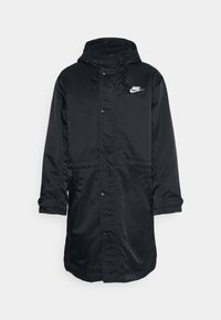 Parka en nylon noir avec capuche, présentant une fermeture éclair sur le devant et des boutons-pression, des poches latérales, et un logo blanc sur la poitrine. Texture lisse.