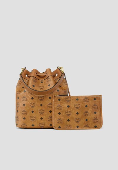 Bruine MCM emmerhandtas en bijpassend etui met rits, voorzien van een zwart logo en diamantpatroon op een grijze achtergrond.