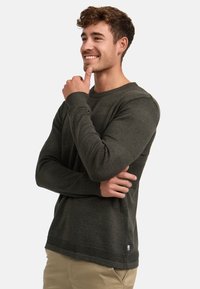 Maglione a maglia verde scuro con motivi testurizzati, scollatura rotonda e polsini a coste. Presenta un'etichetta discreta sull'orlo e una vestibilità comoda.
