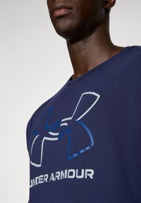 Navy blue t-shirt made of cotton, featuring a large white and blue Under Armour logo on the front and a crew neck design.