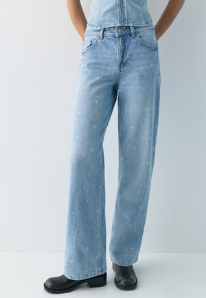 Jean large bleu clair avec de petits motifs de cœurs blancs, porté avec des bottines noires et un haut en denim assorti.