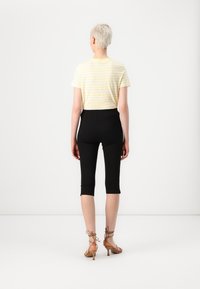 Svarta kortbyxor och en gulrandig t-shirt som visar upp en enkel design, mjuk textur och en figursydd silhuett. Sandaler med remmar i beige.