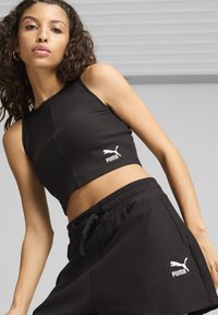 Zwarte geribbelde crop top met een ronde halslijn en het Puma-logo. Gepaard met zwarte shorts met elastische taille, voorzien van zijzakken en logodetail.
