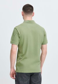 Polo vert en coton texturé avec manches courtes, col plié et étiquette près de l'ourlet, vu de dos.